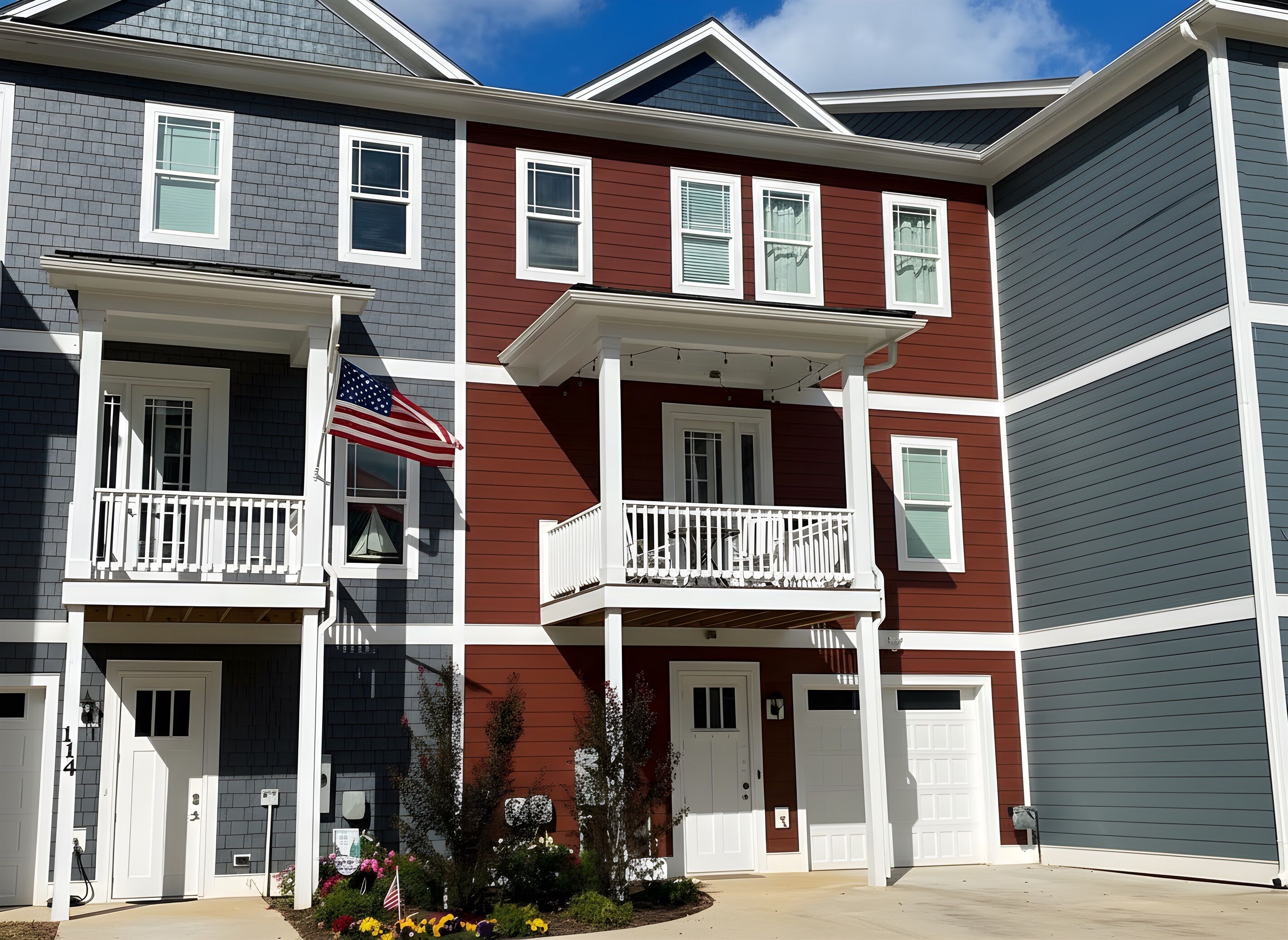 A multi-story residential building with a symmetrical facade, featuring a central entrance with a small porch, white railings, and a flag.