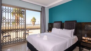 A hotel room with a large bed, a view of the beach, and a balcony with chairs. - Marina Beach Hotel (Tel Aviv)