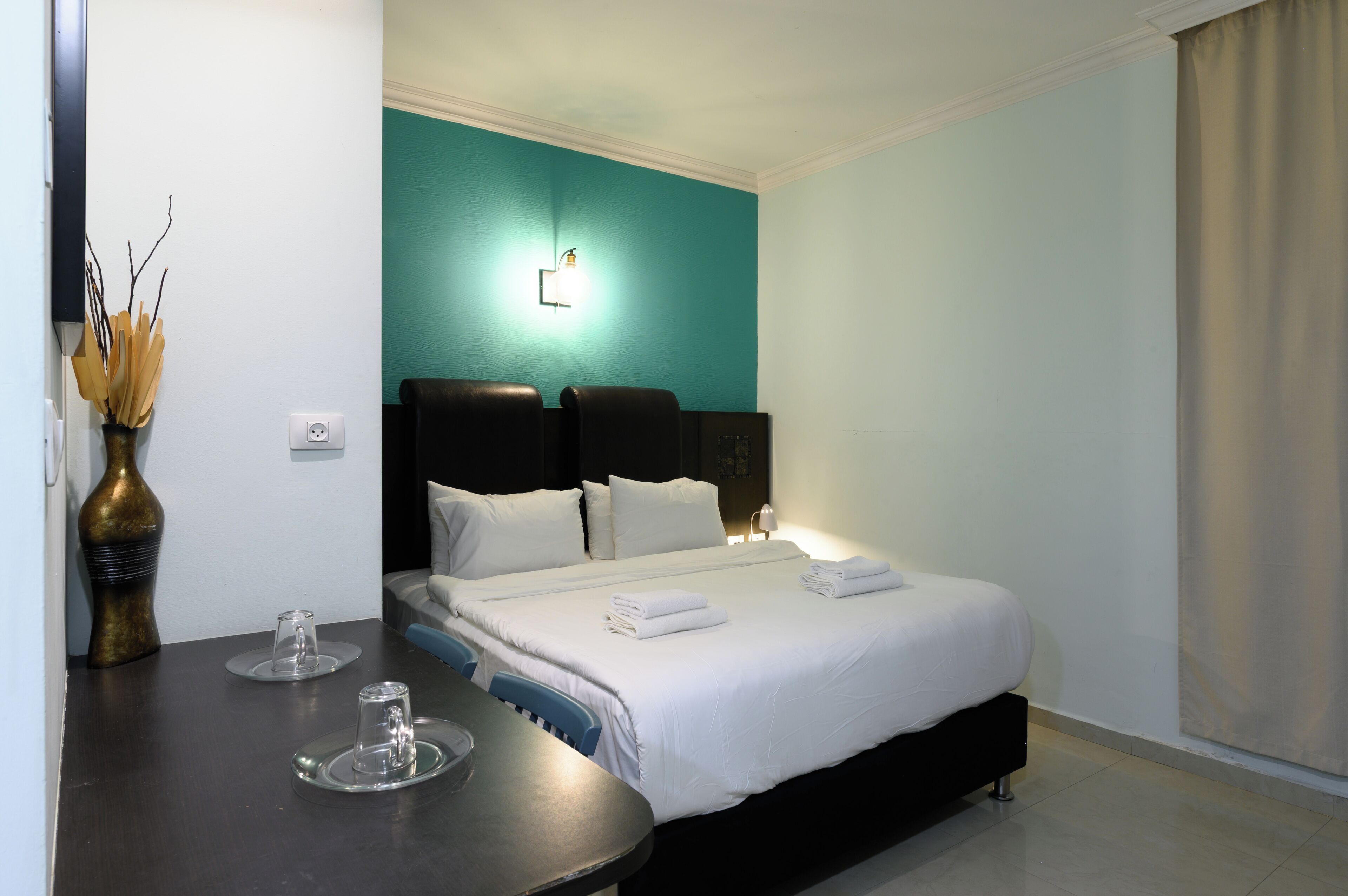 Une chambre d’hôtel avec un lit, des tables de chevet, un vase avec des branches et une lampe fixée au mur.