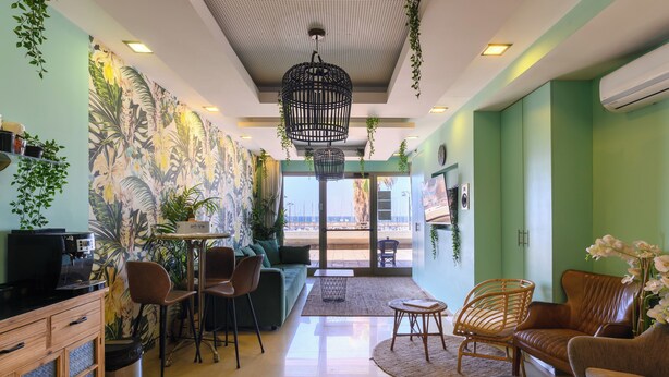 A modern interior with a green wall, tropical wallpaper, a coffee machine, seating area, and a view through a glass door. - Marina Beach Hotel (Tel Aviv)