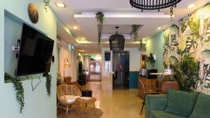 A spacious living area with a green sofa, wicker chairs, a flat-screen TV, and a ceiling fan. - Marina Beach Hotel (Tel Aviv)