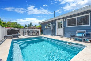 Una piscina con zona de estar cubierta y una casa con garaje.