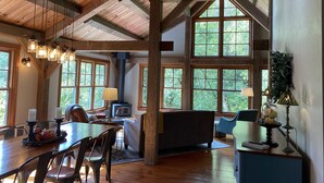 A spacious room with a high ceiling, wooden beams, large windows, a fireplace, and a dining area with a table and chairs. - Escape the hustle and bustle and unwind at RIVERLOFT! Tranquility Awaits! (Scio)