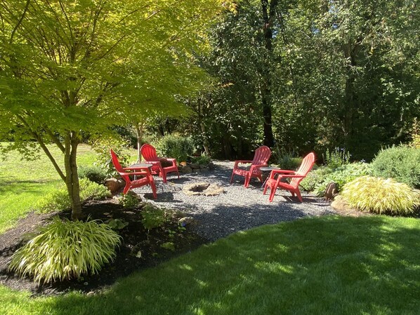 A garden patio with red chairs and a table, surrounded by lush greenery and trees. - Escape the hustle and bustle and unwind at RIVERLOFT! Tranquility Awaits! (Scio)