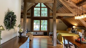 A spacious attic bedroom with exposed wooden beams, large windows, a wooden dining table, and a cozy bed area. - Escape the hustle and bustle and unwind at RIVERLOFT! Tranquility Awaits! (Scio)