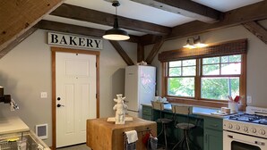 A kitchen with a sign reading "BAKERY" above the door, a refrigerator, a stove, and a window with a view of greenery. - Escape the hustle and bustle and unwind at RIVERLOFT! Tranquility Awaits! (Scio)