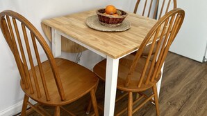 A dining table with four wooden chairs, a woven basket with oranges, and a white refrigerator in the background. - Be our guest at The Nest!  (Pleasant Valley)