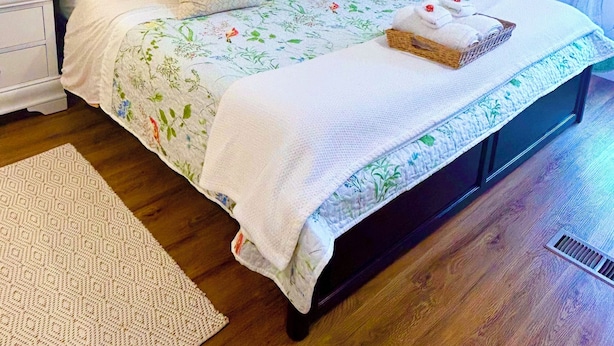 A neatly made bed with floral bedding, a bedside table with a lamp, and a bedside basket. - Be our guest at The Nest!  (Pleasant Valley)