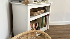 A white entertainment unit with a flat-screen TV, a decorative bowl, and a candle. Below, there are books and a woven basket. - Be our guest at The Nest!  (Pleasant Valley)