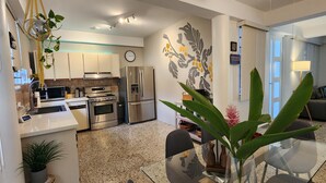 A modern kitchen with stainless steel appliances, a dining area with a glass table, and a living space with a sofa and a plant. - San Juan Charm • ForestEdge Retreat • Gated Privacy Near Beach, Airport & Old SJ (San Juan)
