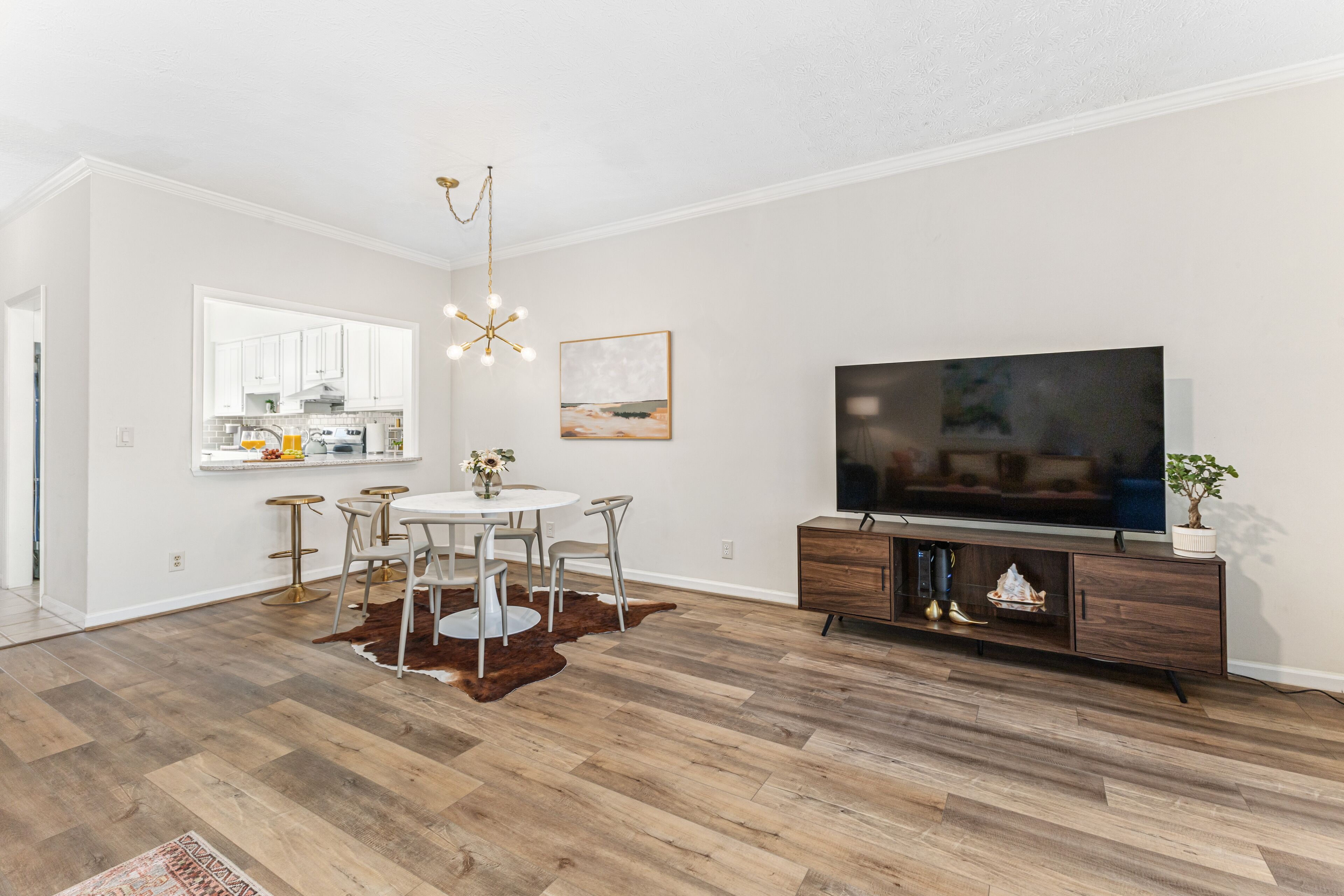 A modern living room with a dining area, a flat-screen TV, and a wooden floor.