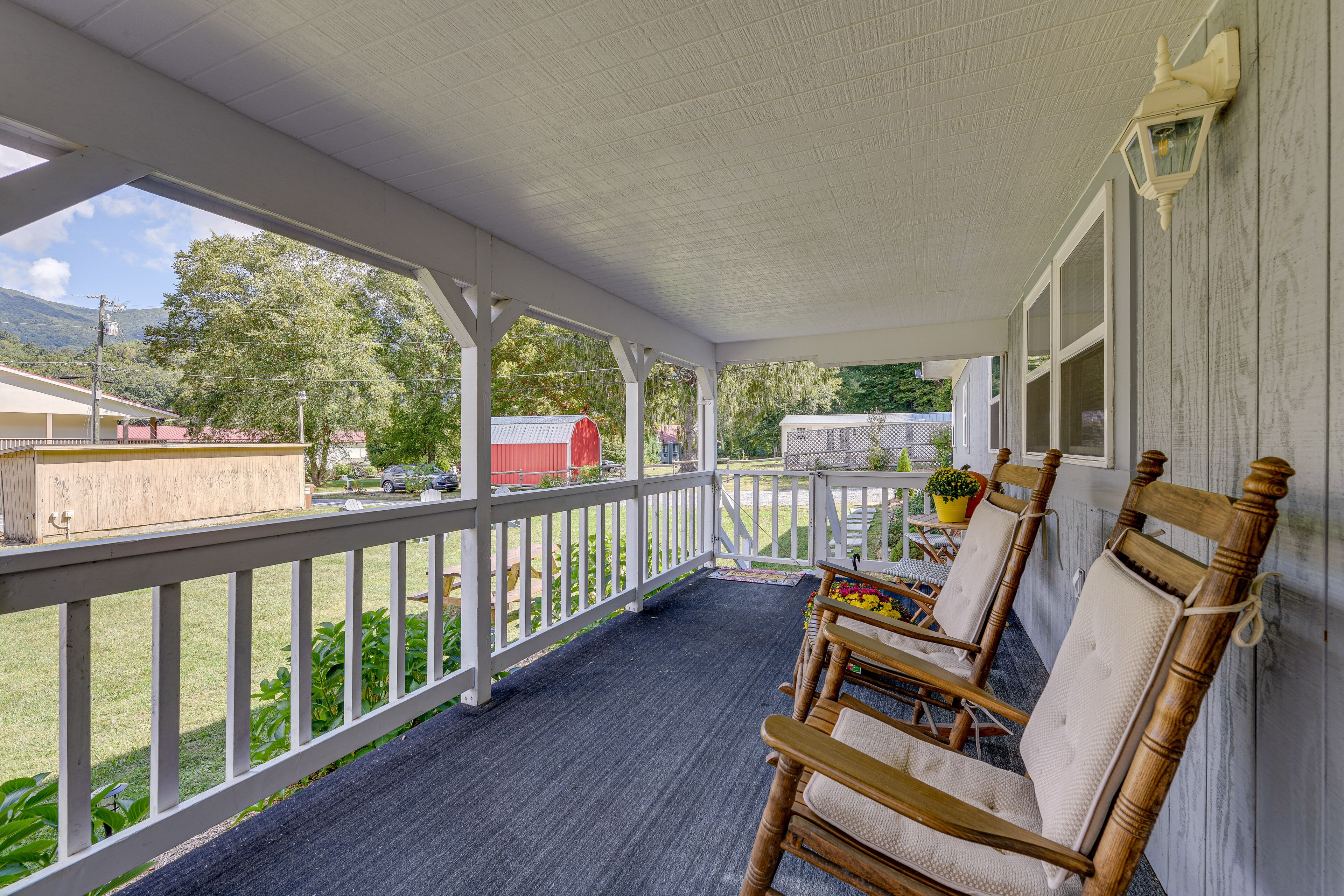 A covered porch with a view of a rural landscape, wooden chairs, and a small table.