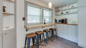 A kitchen with a bar area, wooden stools, white cabinets, and a hanging light fixture. - 5 Mi to Cataloochee Ski Area! Family Home w/ Views (Maggie Valley)