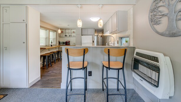 A kitchen with two bar stools, a white refrigerator, and a wall-mounted heater. - 5 Mi to Cataloochee Ski Area! Family Home w/ Views (Maggie Valley)