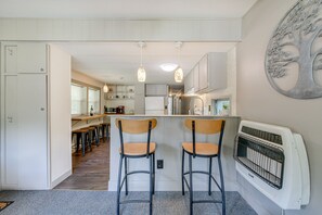A kitchen with two bar stools, a white refrigerator, and a wall-mounted heater. - 5 Mi to Cataloochee Ski Area! Family Home w/ Views (Maggie Valley)