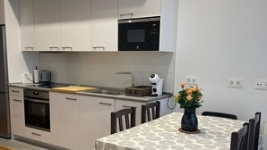 Une cuisine moderne avec des meubles blancs, un four à micro-ondes encastré et un coin repas avec une table recouverte d’une nappe à motifs.