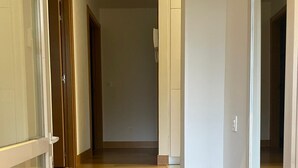 Un couloir au sol en bois et aux murs blancs, qui mène à une pièce dotée d’une porte.