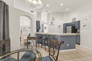 A modern kitchen with a central island, bar stools, and a dining area with a glass table.