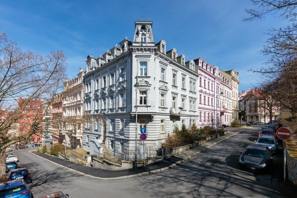A historic building with classical architecture, a corner entrance, and parked cars along the street.