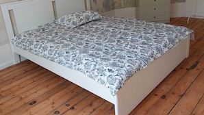 Une chambre avec un lit blanc, un plancher en bois et une commode blanche.