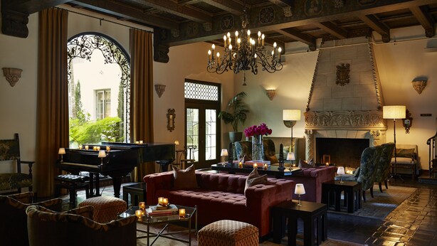 A grand room with a grand piano, a plush red sofa, and a chandelier.