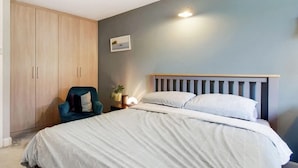 A bedroom with a bed, a chair, a wardrobe, and a wall-mounted picture. - Bakersfield (London)