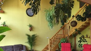 A living room with a sofa, chairs, a staircase, and various potted plants.