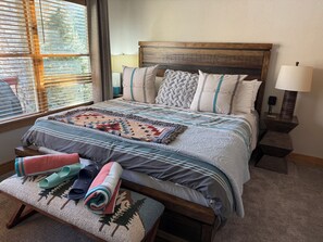 Un letto rifatto con cura, coperto da una coperta fantasia, cuscini e una lampada da comodino.