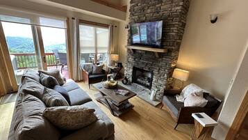 Una sala de estar acogedora con chimenea de piedra, un sofá confortable y un televisor montado en la pared.