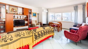 Una sala de estar con un sofá, un sillón rojo, un televisor y un comedor con una mesa y sillas.