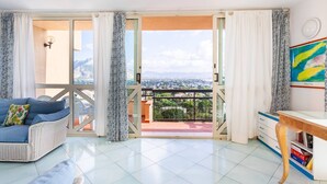 Un balcón con vistas a un paisaje urbano, un sofá de mimbre, un escritorio de madera y una estantería.