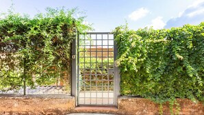 Una entrada protegida por un portón metálico, rodeada de abundante vegetación y un camino de hormigón.