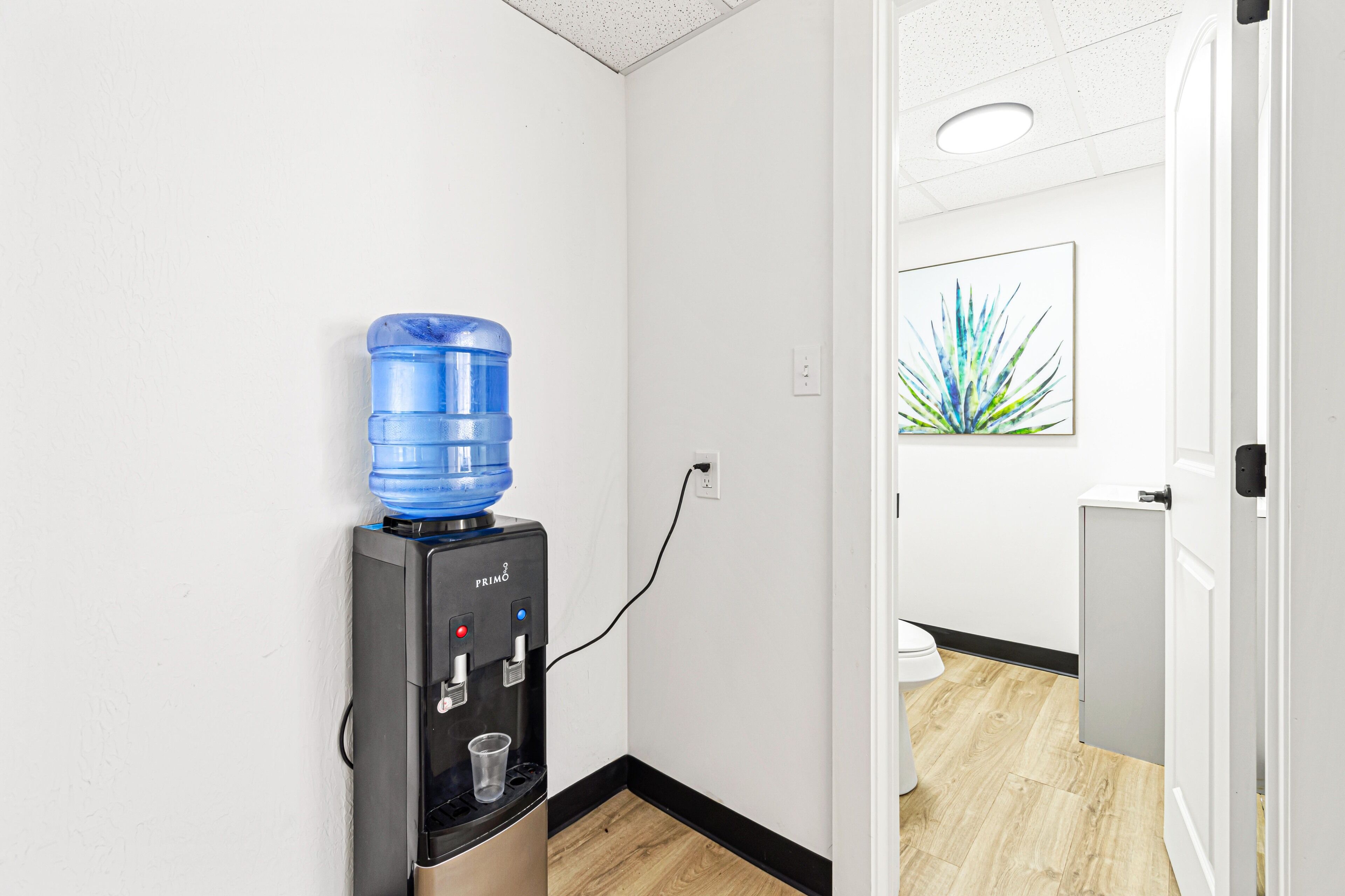 A water dispenser in a hallway with a wooden floor and a white wall.