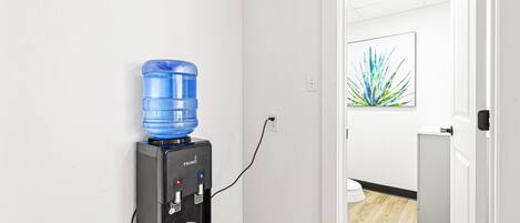A water dispenser in a hallway with a wooden floor and a white wall.