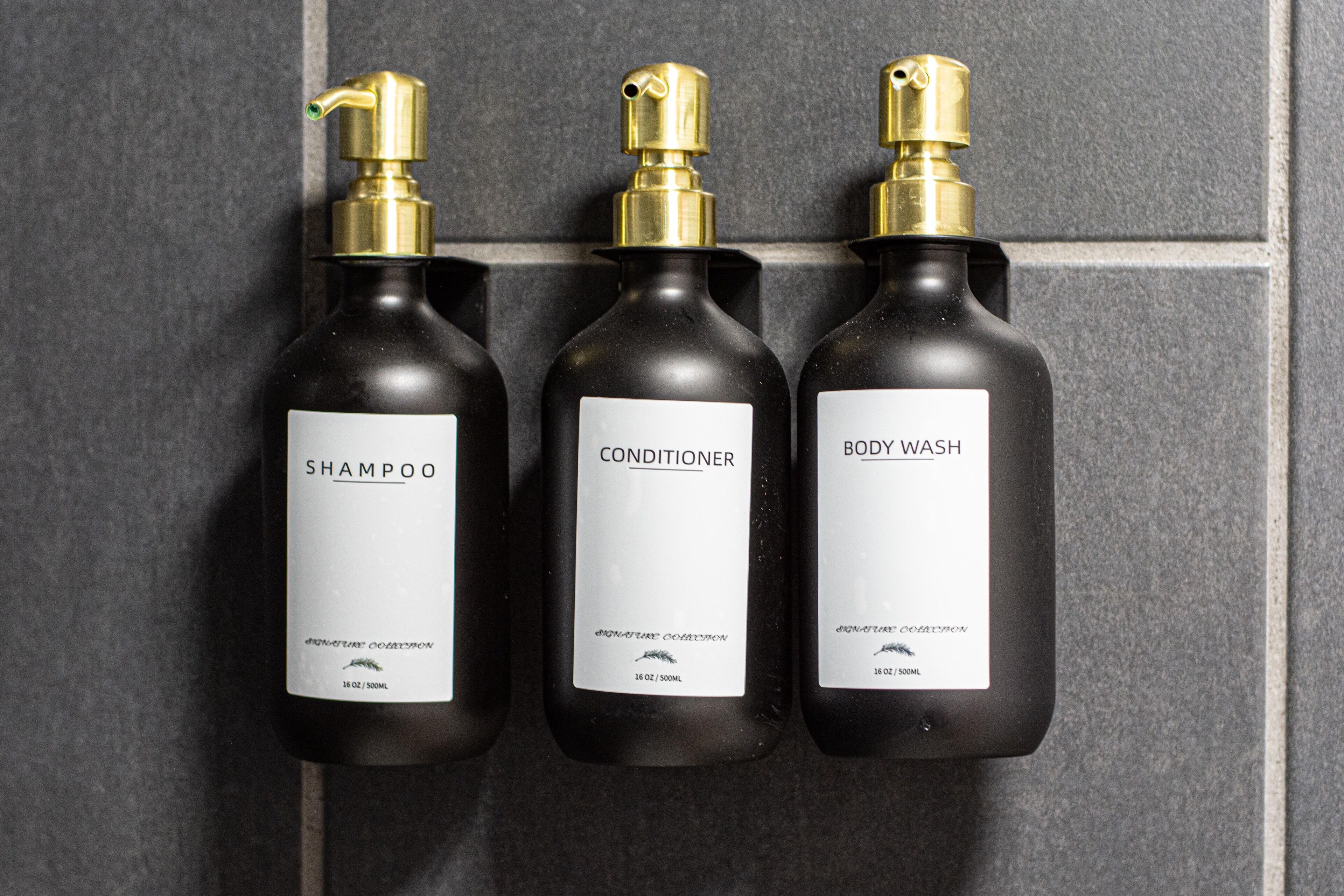 Trois flacons de produits d’hygiène personnelle dotés de pompes doseuses, étiquetés « shampoing », « après-shampoing » et « gel douche », chacun contenant 16 oz / 500 ml.