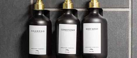 Drie flessen persoonlijke verzorgingsproducten met pompdop, gelabeld als shampoo, conditioner en douchegel, elk met een inhoud van 16 oz / 500 ml.