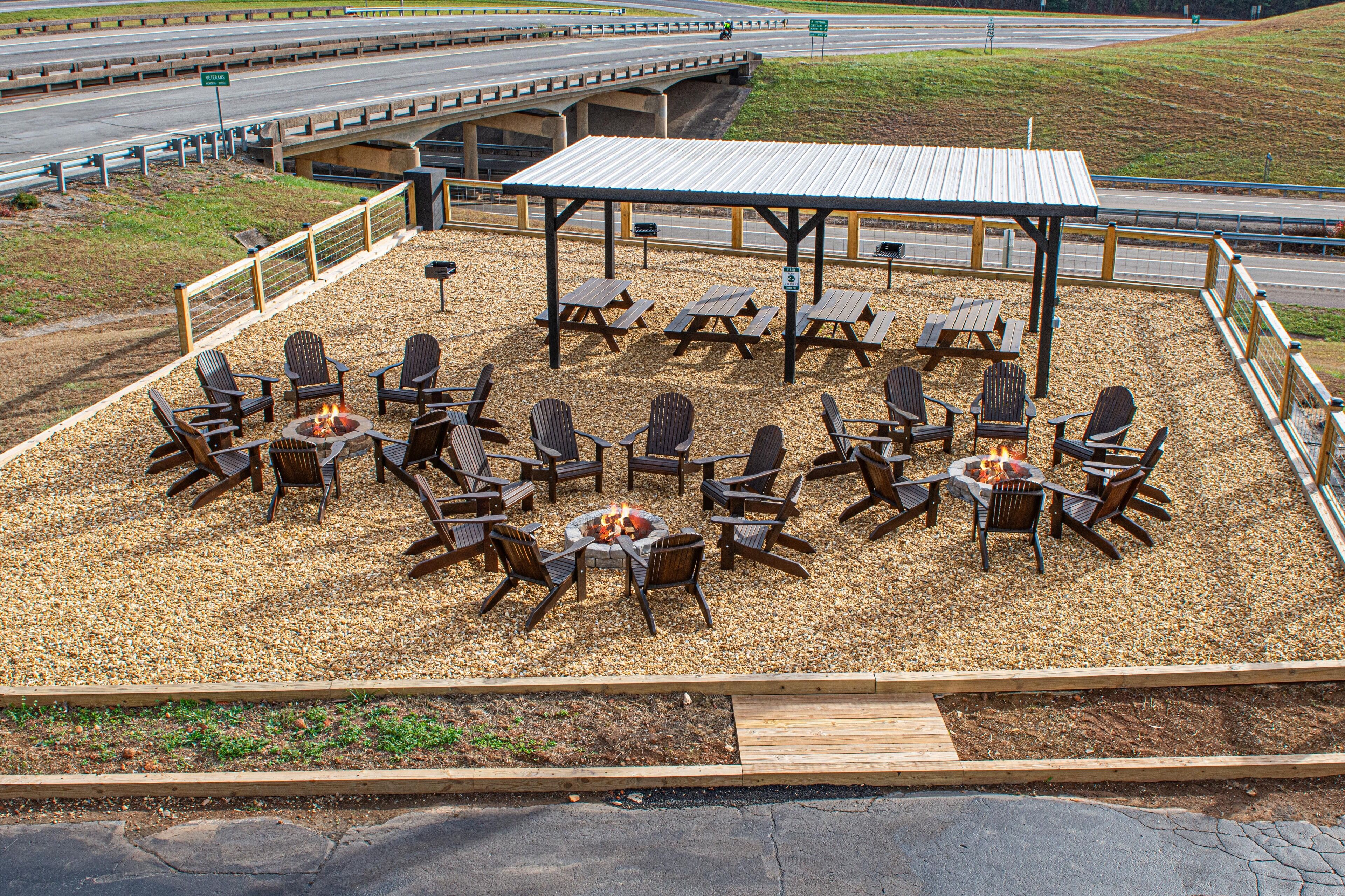 An outdoor seating area with fire pits and picnic tables, surrounded by chairs and a covered pavilion.