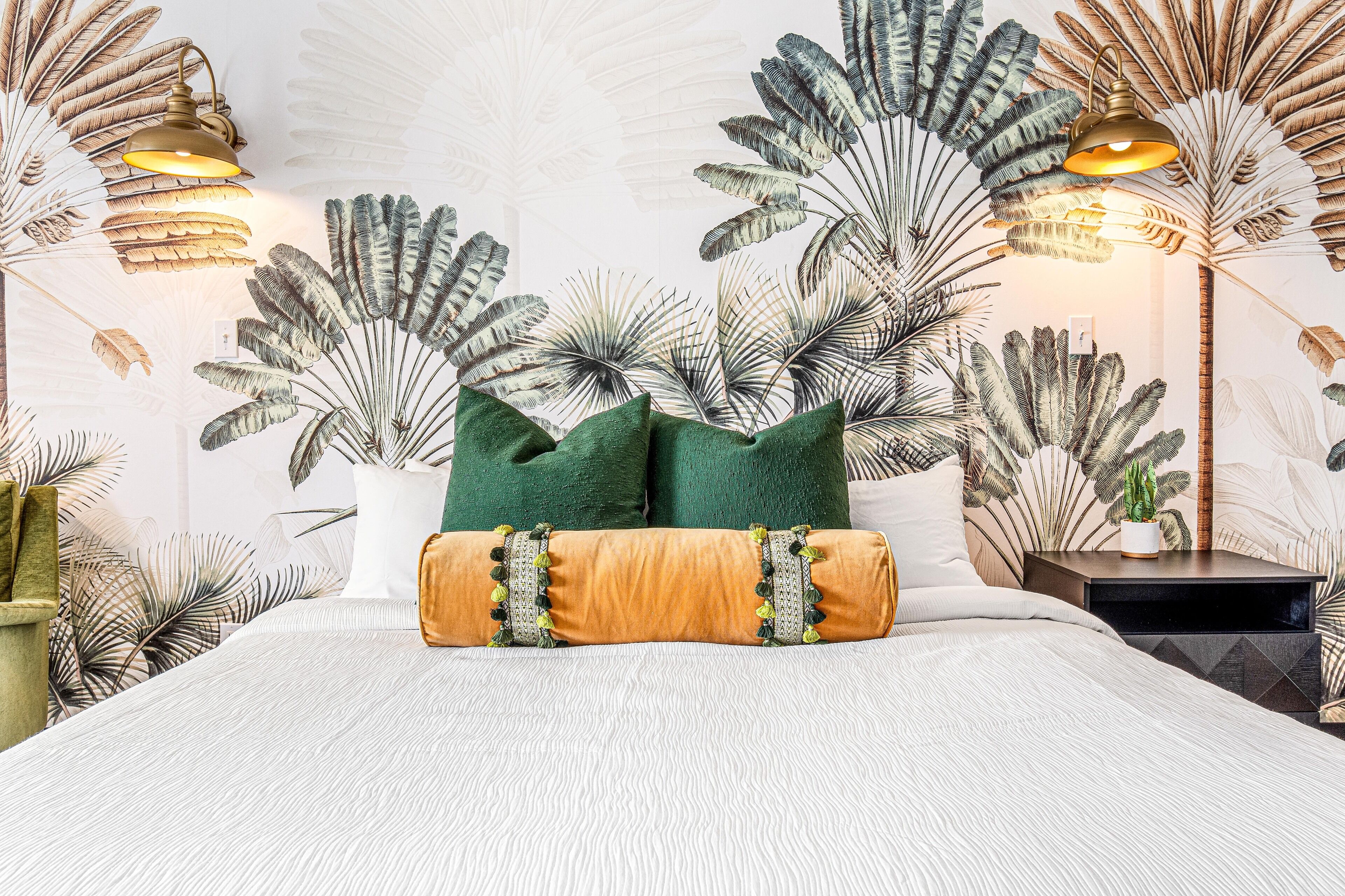 Une chambre à coucher avec un lit, des oreillers verts et bruns, une table de chevet et des lampes fixées au mur.