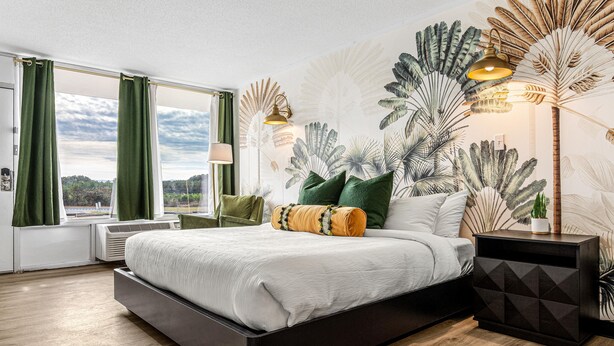 A modern bedroom with a large bed, green curtains, a wall mural, and a nightstand. - The Mallard Hotel (Copperhill)