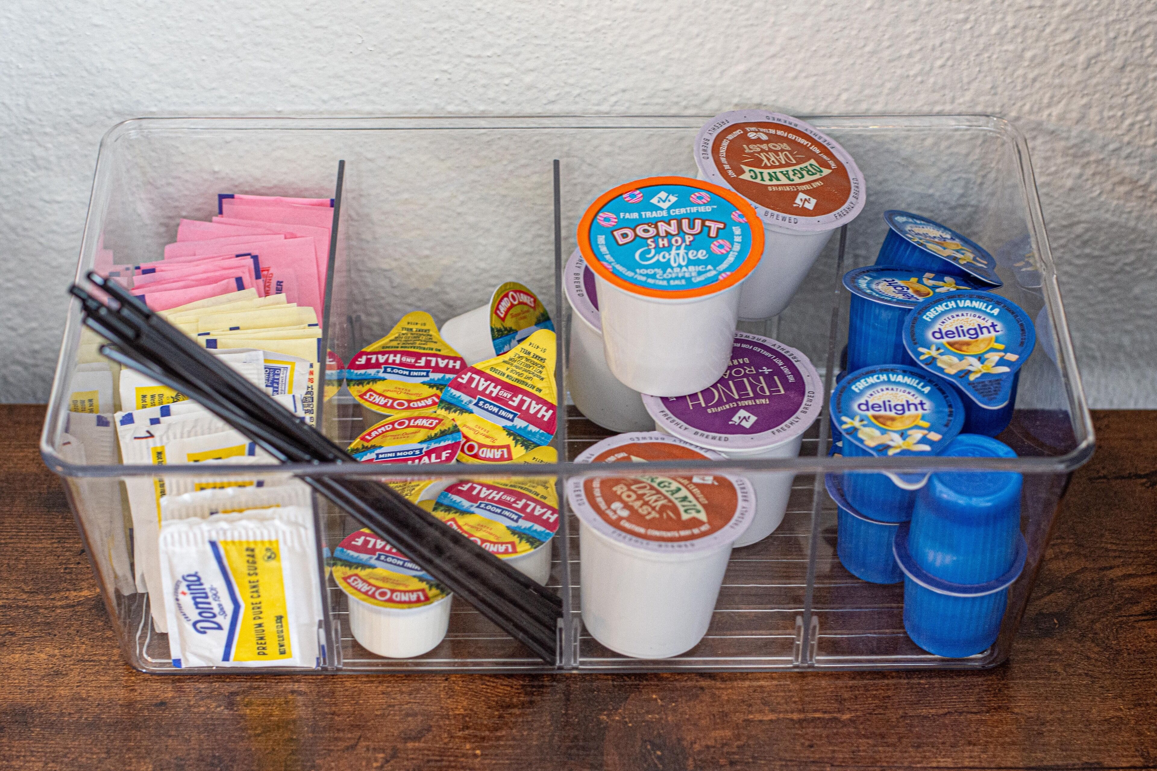 Un contenedor de almacenamiento con diversos alimentos, como vasitos de yogur, sobrecitos de azúcar y etiquetas de comida.