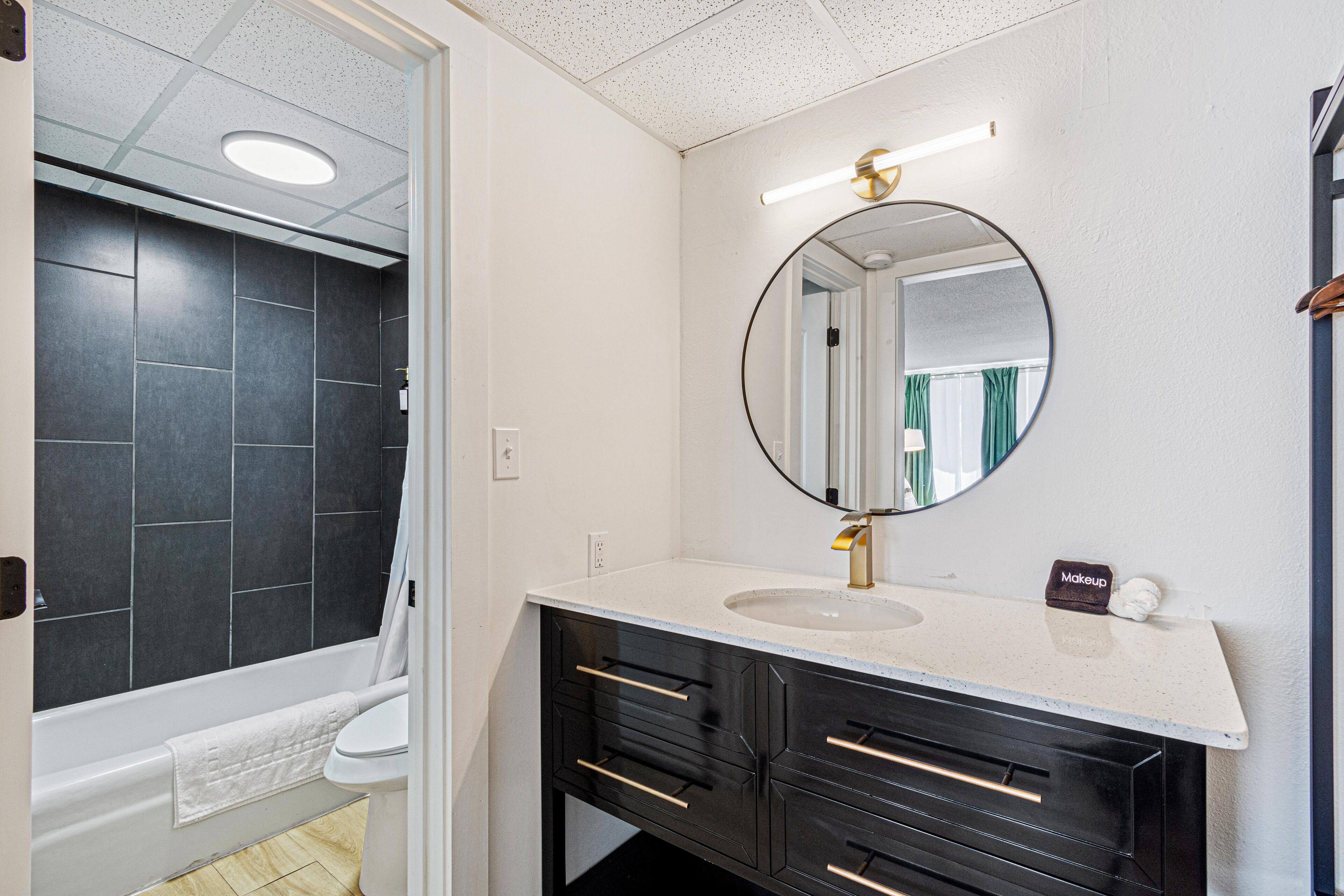 Un baño moderno con bañera, lavamanos con espejo redondo y muebles oscuros.