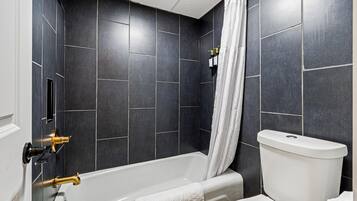 A modern bathroom with dark tiles, a white bathtub, a white toilet, and a shower curtain.