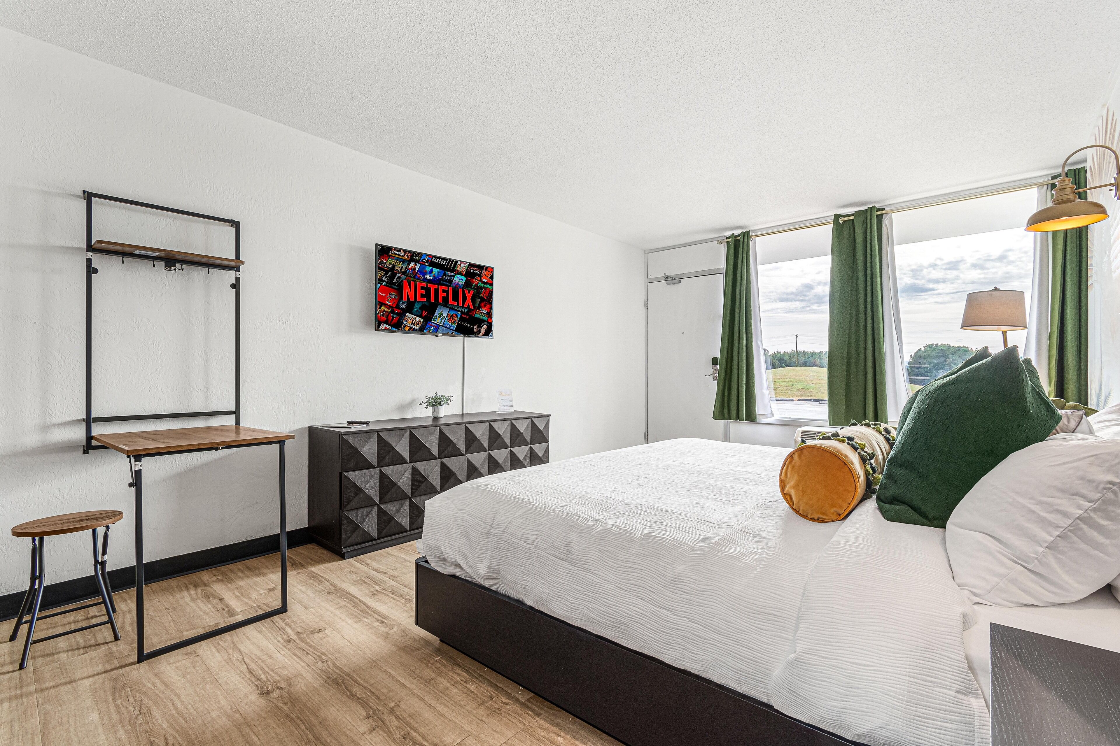A modern bedroom with a bed, a desk, a dresser, and a wall-mounted TV displaying the Netflix logo.