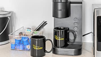 En kaffemaskine, en kop og en beholder med blå kopper på en bordplade.
