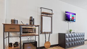 A modern hotel room with a kitchenette, a flat-screen TV mounted on the wall, and a bed with a white comforter. - The Mallard Hotel (Copperhill)
