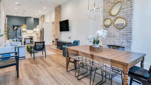 Un salon moderne avec une table à manger en bois, des canapés et un téléviseur fixé au mur.