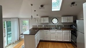 A kitchen with white cabinets, a black countertop, a skylight, and a view of the outdoors. - Sunset Studio (Branford)