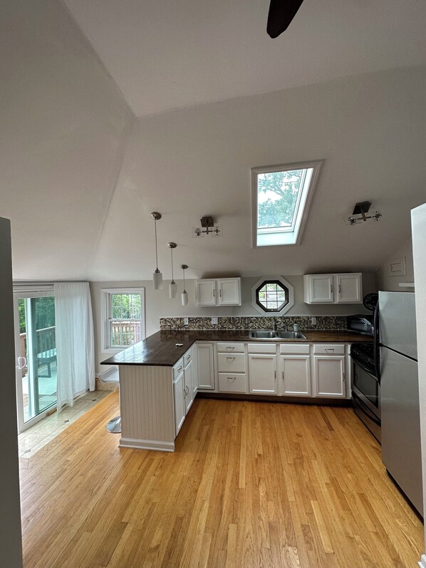 A kitchen with white cabinets, a black countertop, a skylight, and a view of the outdoors.