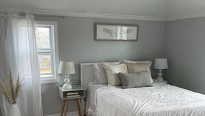 A bedroom with a bed, bedside tables, a window with curtains, a wall-mounted picture, and a fluffy rug. - Sunset Studio (Branford)