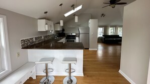 A spacious kitchen with a central island, two bar stools, and a ceiling fan. - Sunset Studio (Branford)